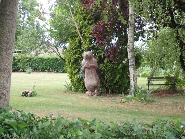 Wooden bear sculpture in garden with surrounding trees.