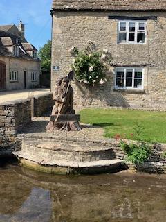Stone statue beside traditional stone house and pond.