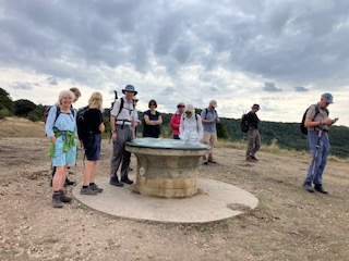 Hikers gathered around stone marker on hilltop.