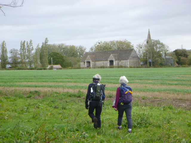 Walkers approaching barn in green countryside landscape.