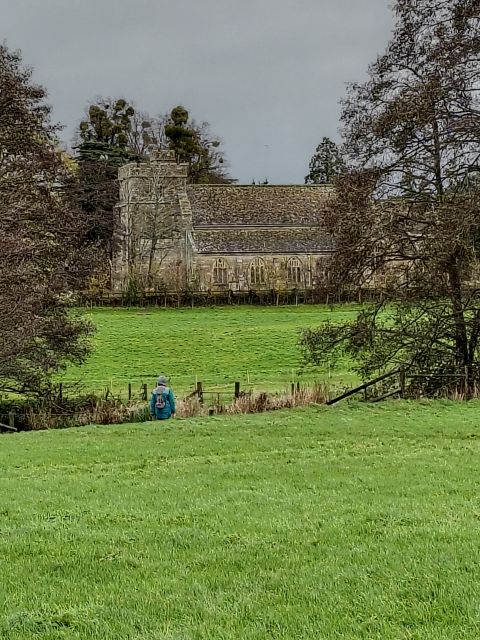 Woman walking towards old church across green field.