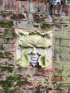Stone face sculpture on mossy brick wall