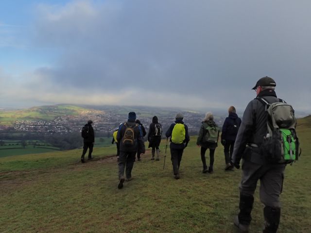 Group hiking on a grassy hill under cloudy sky.