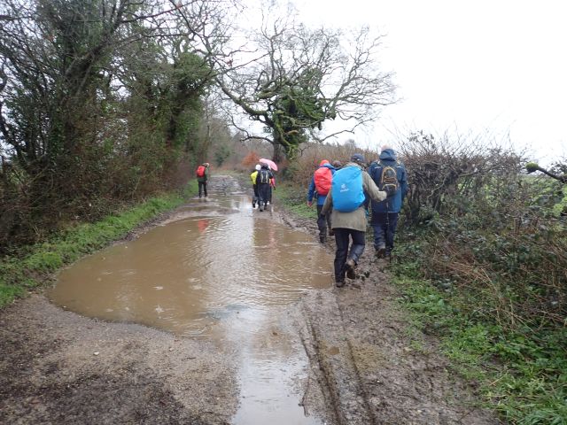 Hikers navigating muddy country path in rain.