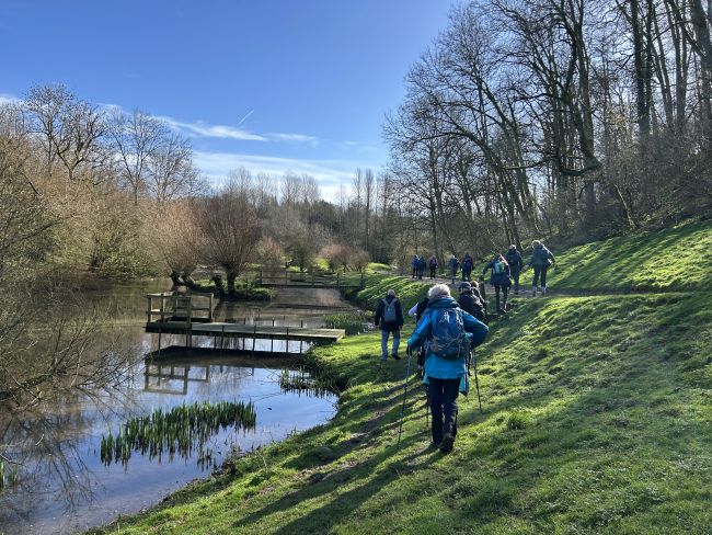 Group hiking beside a river in winter sun.